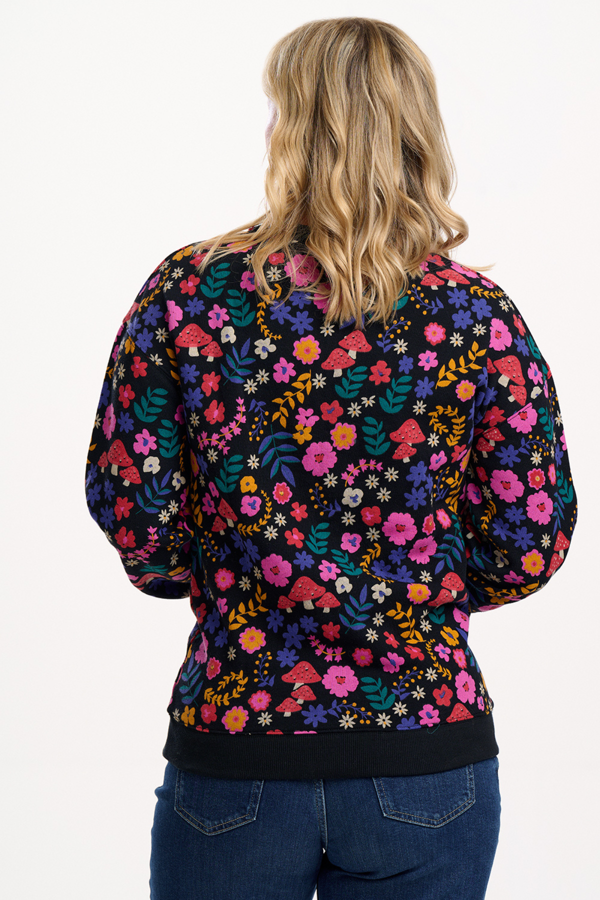 Blond model i sweatshirt med blomsterprint og svampe – set bagfra, viser rygdetaljer.