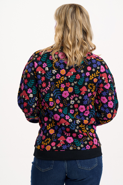 Blond model i sweatshirt med blomsterprint og svampe – set bagfra, viser rygdetaljer.