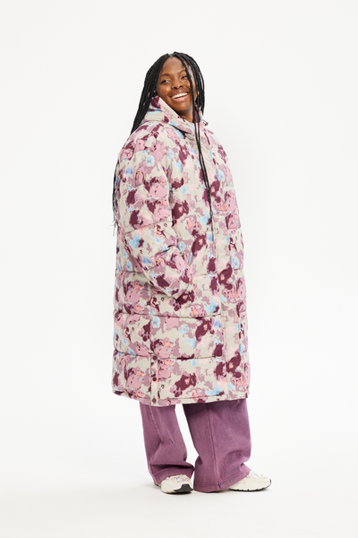 Model smilende i lang Amber vinterjakke med pink-lilla mønster, set fra skrå vinkel