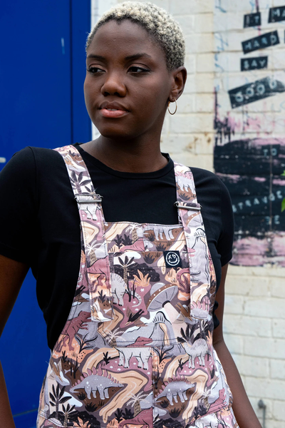 Nærbillede af model i Rebel Romance Dinoverse dungarees, der viser printet med dinosaurer og vulkaner på bryststykket.