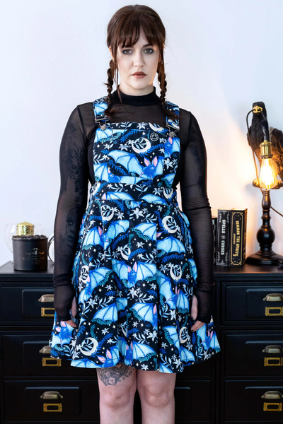 Model i Rebel Romance Night Flight Pinafore med blå flagermus og måneprint, iført sort meshbluse.