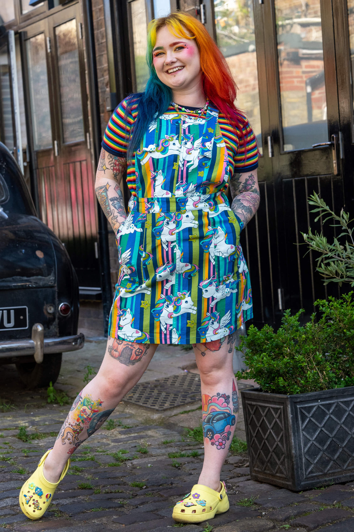 Fuld figur af model i farverig smækkjole fra RUN&FLY – regnbuehår, tattoos og gule crocs