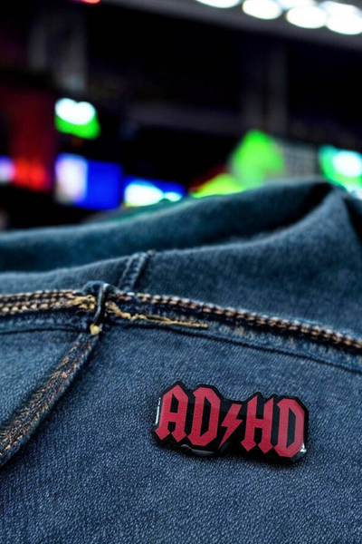 Pin fastgjort på mørk denimjakke, fotograferet med farvede lys i baggrunden.