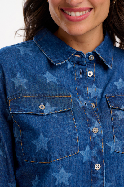 Close-up af denimskjorte med stjerneprint, synlige knapper og brystlommer med knaplukning.