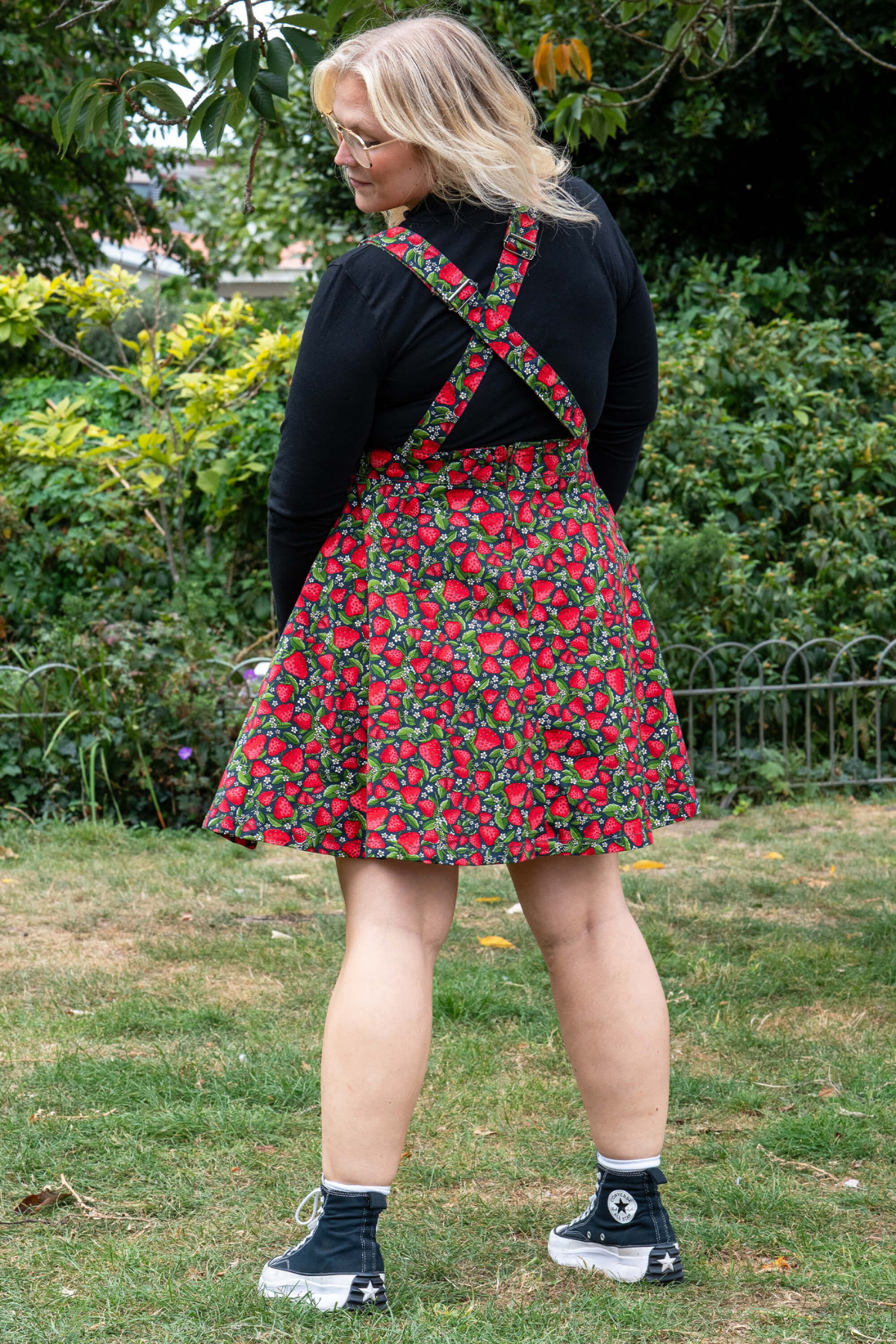Bagfra visning af Rebel Romance Strawberry Field Pinafore med krydsede stropper og jordbærmønster.