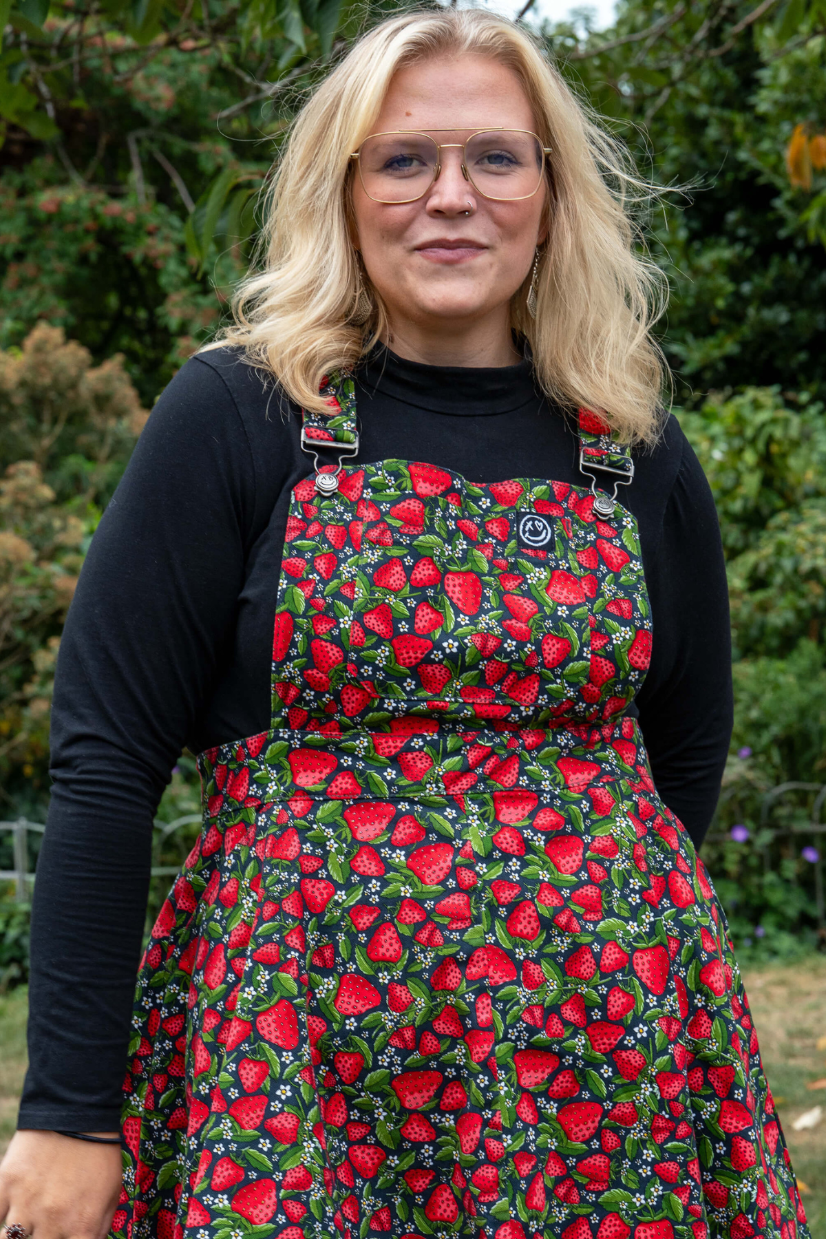Model i Rebel Romance Strawberry Field Pinafore med farverigt jordbærprint og sort bluse.