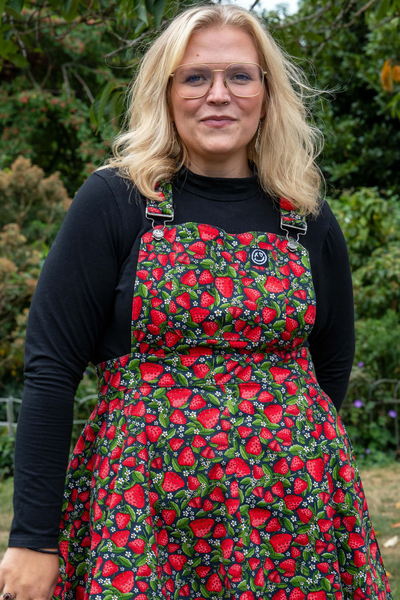 Model i Rebel Romance Strawberry Field Pinafore med farverigt jordbærprint og sort bluse.