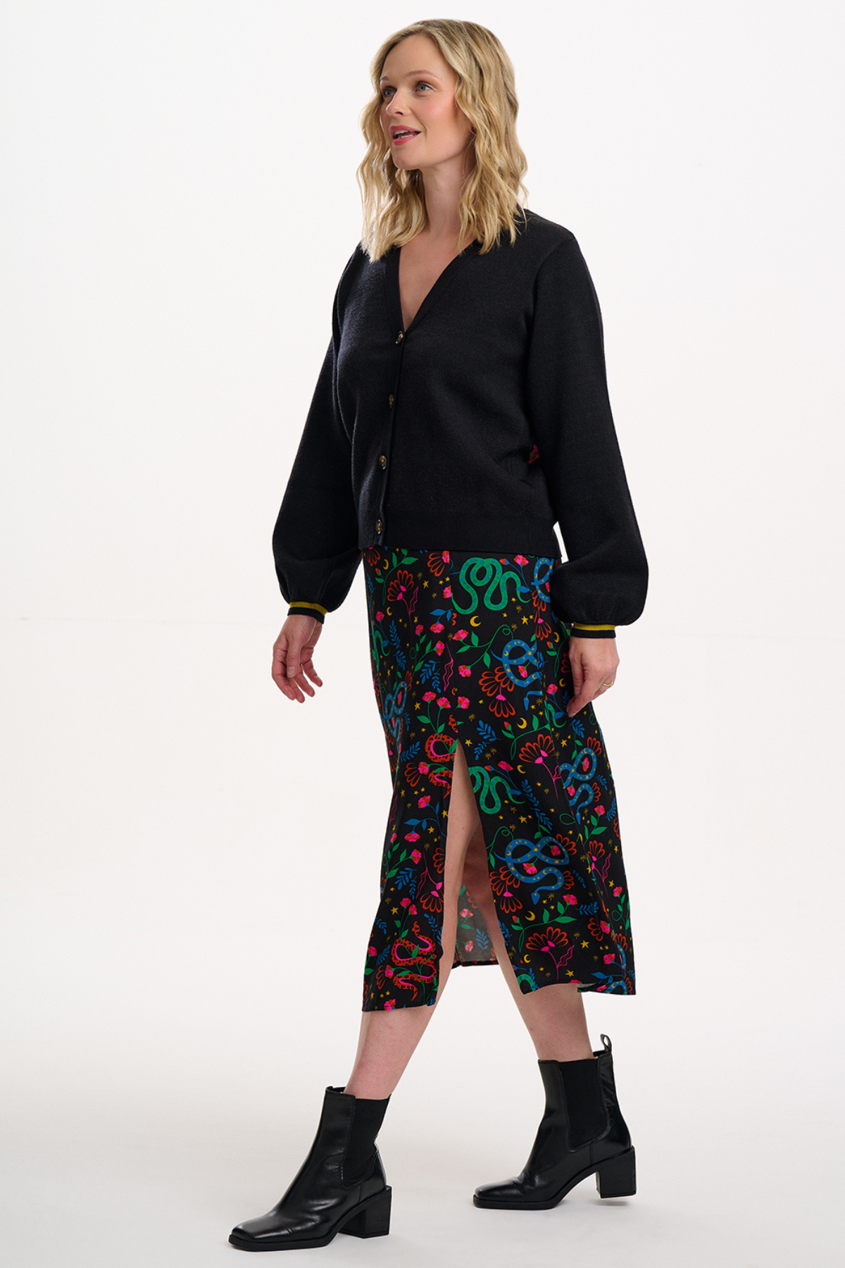 Model i Rosalind Skirt stylet med sort cardigan og støvler – set fra siden