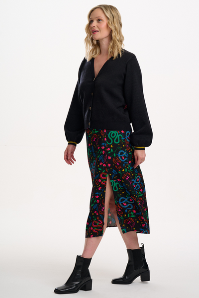 Model i Rosalind Skirt stylet med sort cardigan og støvler – set fra siden