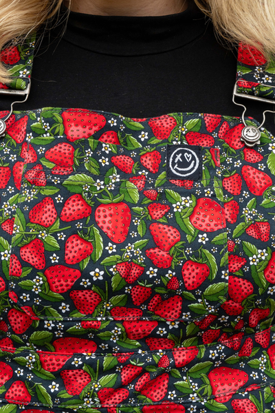 Nærbillede af model i Rebel Romance Strawberry Field Pinafore – fokus på bib-lommen og jordbærprintet.