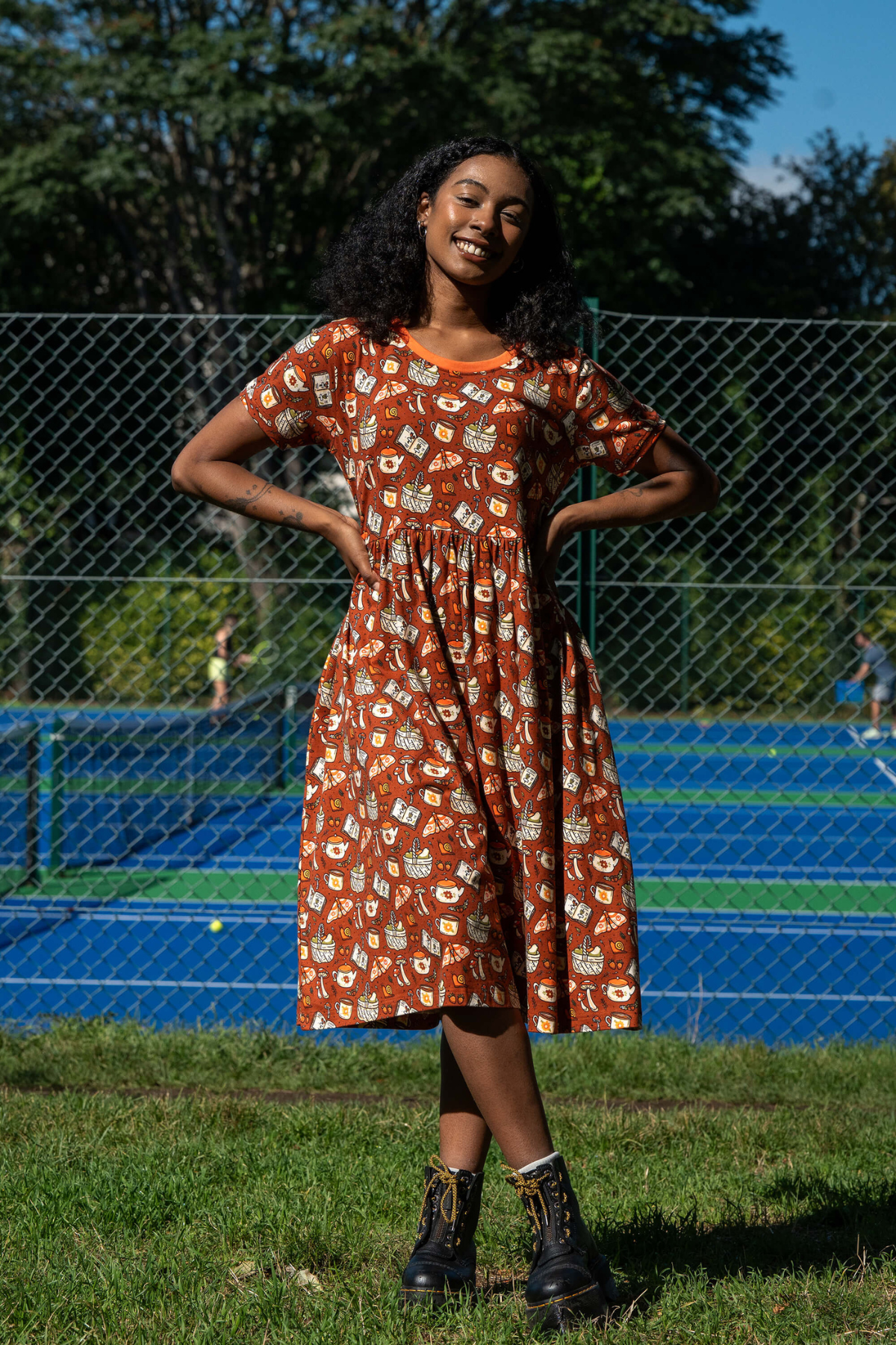 Rebel Romance Mushroom Tea Party midi smockkjole med orange kant og cottagecore print af svampe, bøger og tekrus.
