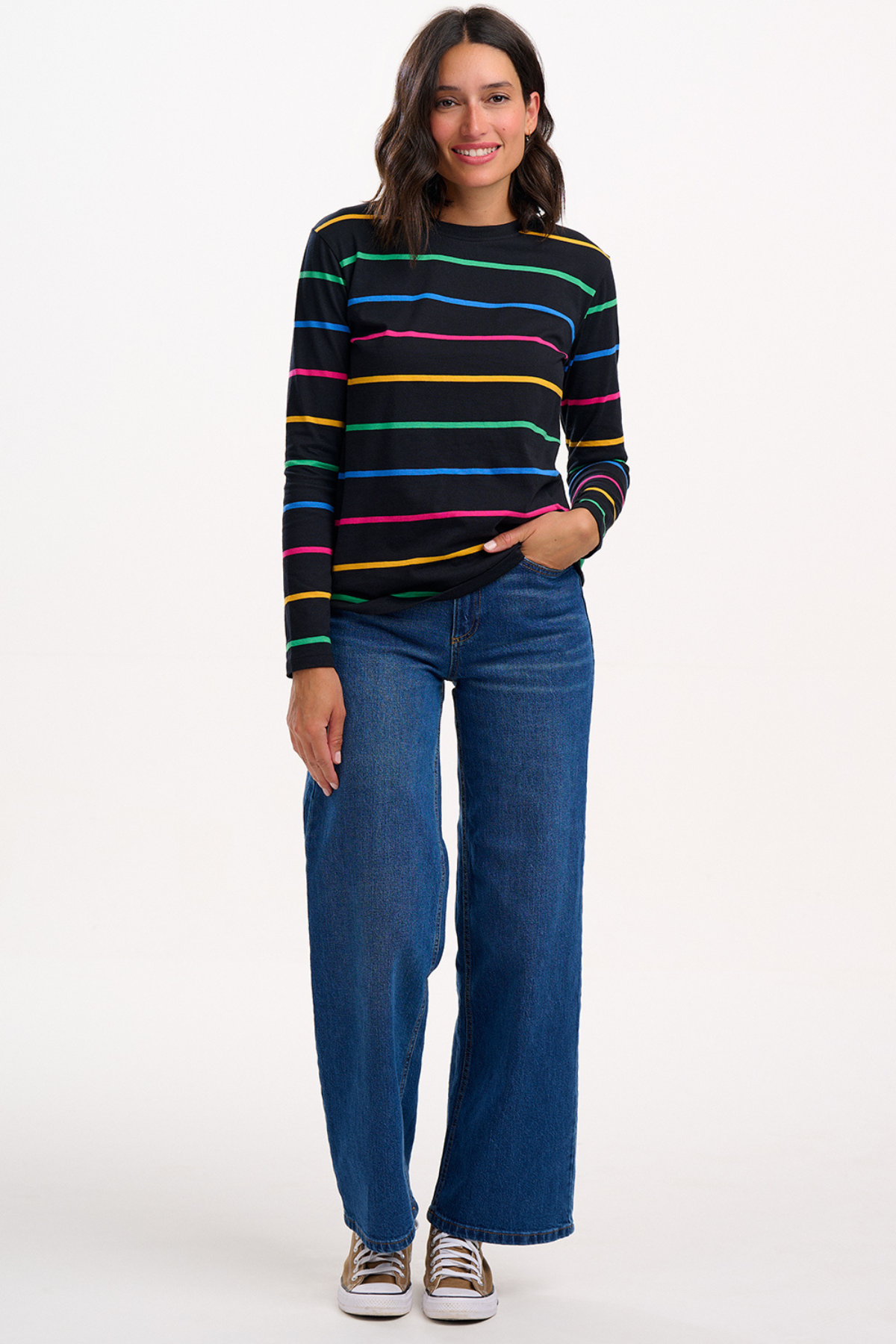 Model i fuld figur iført Brunswick Jersey Top og blå jeans, hænderne afslappet i lommen.