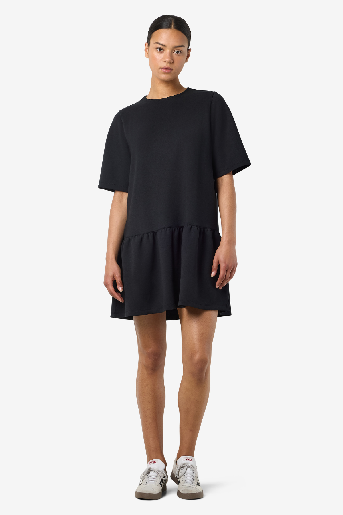Fuld figur: Model iført kort sort kjole fra Noisy May stylet med hvide sneakers og afslappet holdning