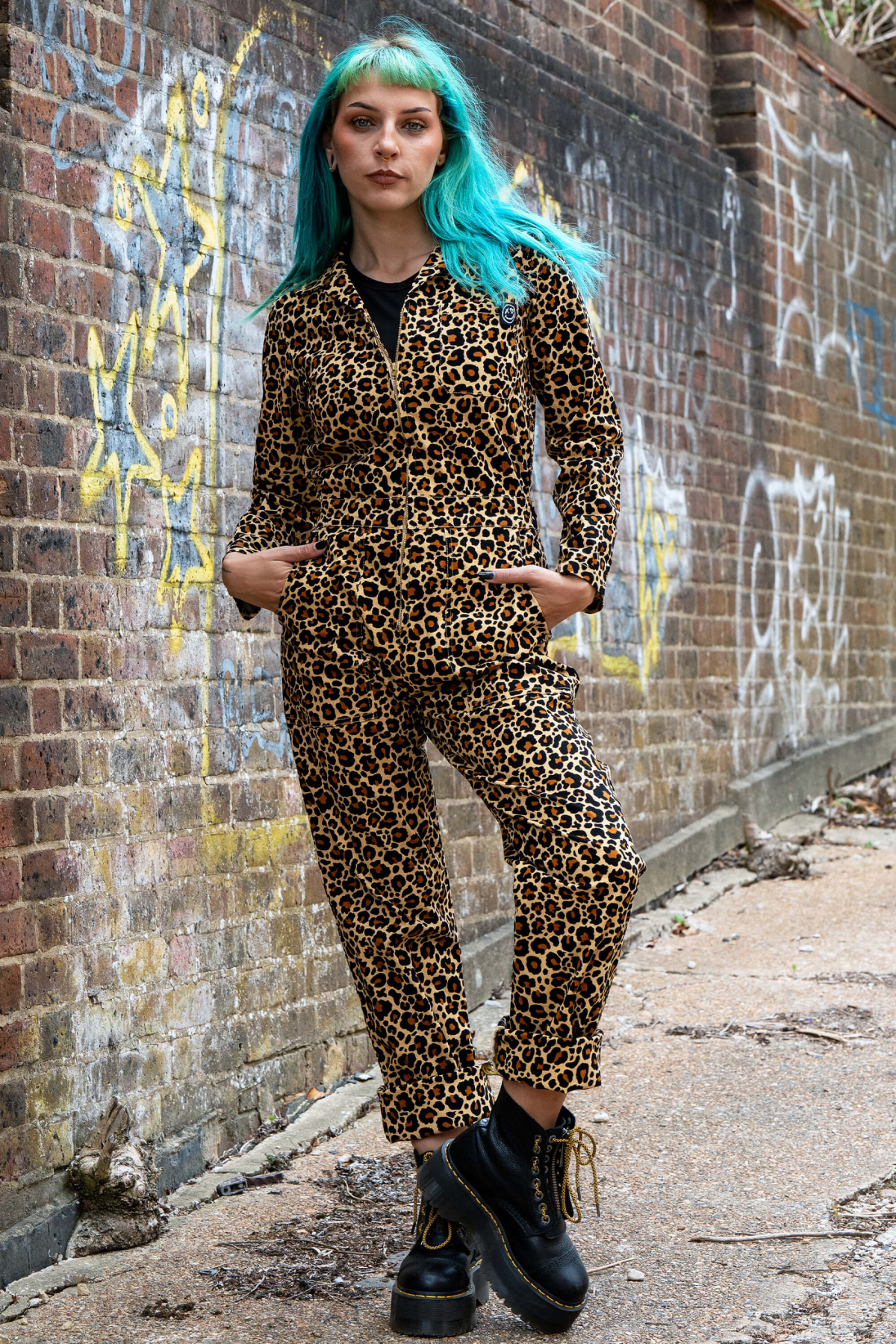Model i Rebel Romance Leopard Boiler Suit med klassisk leopardprint og sorte støvler foran mur med graffiti.