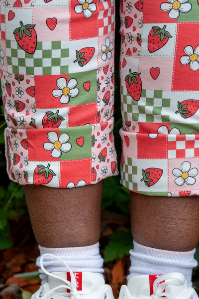 Nærbillede af buksebenet på Strawberry Picnic Dungarees, der viser jordbær, blomster og tern.