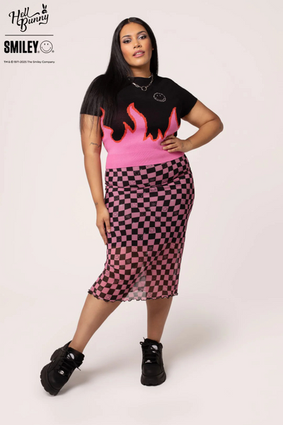 Plus size model i Distortion Skirt og Dylan Top, frontalt med hånd på hoften, smilende.