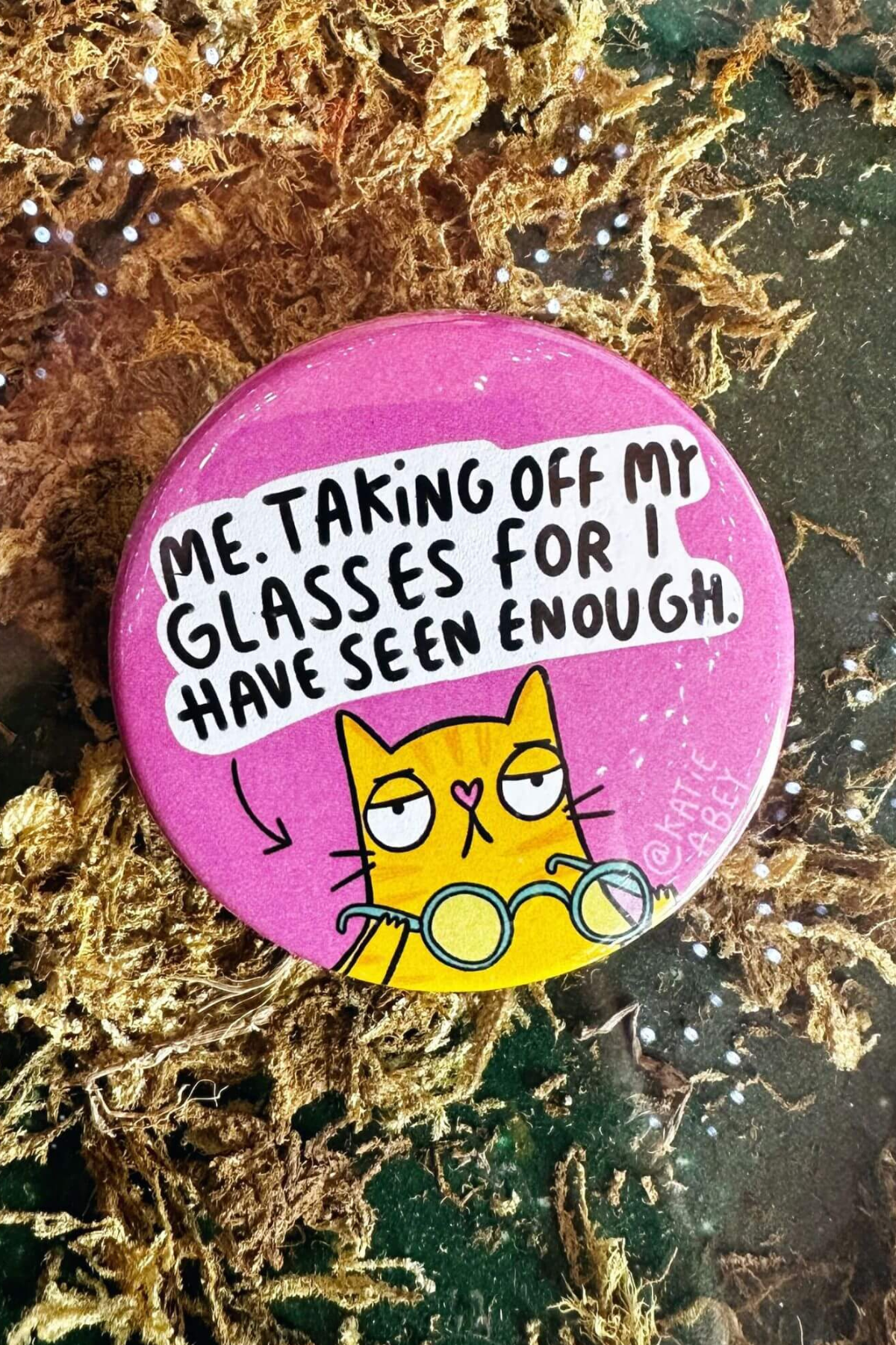 Sjov badge med gul kat og relaterbar tekst på pink baggrund