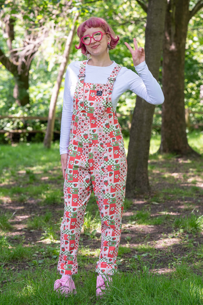 @fairyjesss står i sollys i Strawberry Picnic Dungarees, smilende og iført pink briller.