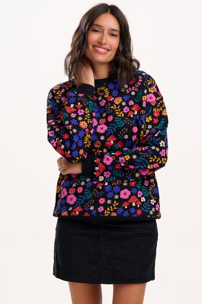 Model i sort sweatshirt med farverigt blomster- og svampeprint fra Sugarhill Brighton – set forfra, smilende.