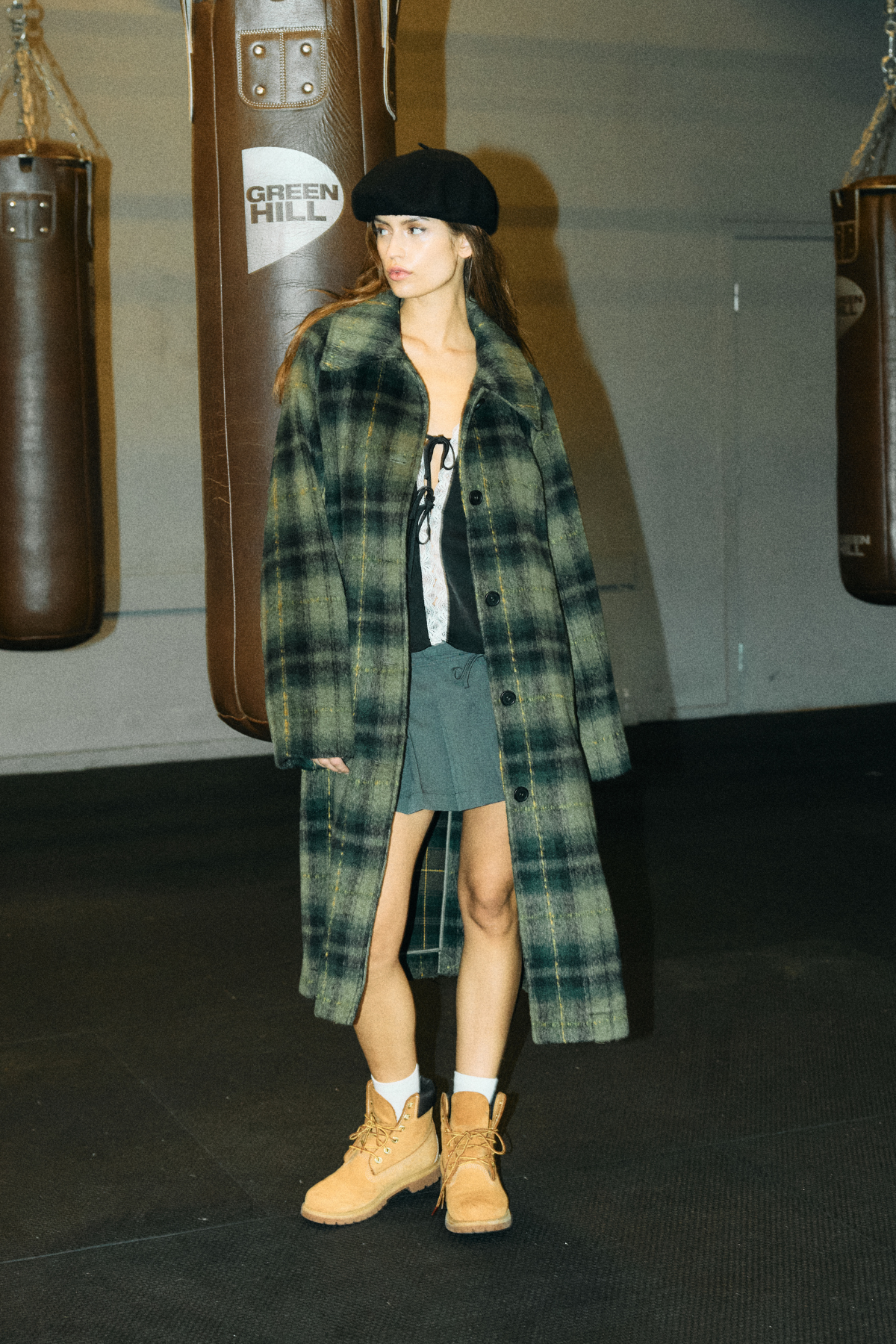 Model i lookbook iført NOISY MAY CHRISTINA lang ternet frakke i grøn – styled med sort baret og støvler.