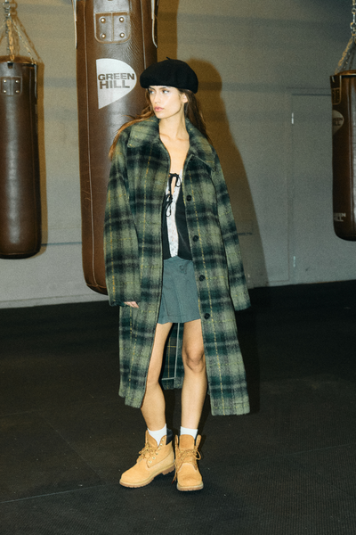Model i lookbook iført NOISY MAY CHRISTINA lang ternet frakke i grøn – styled med sort baret og støvler.