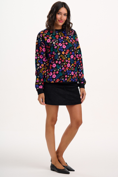 Model i sort sweatshirt med farverige blomster og svampeprint – poserer afslappet, set forfra.