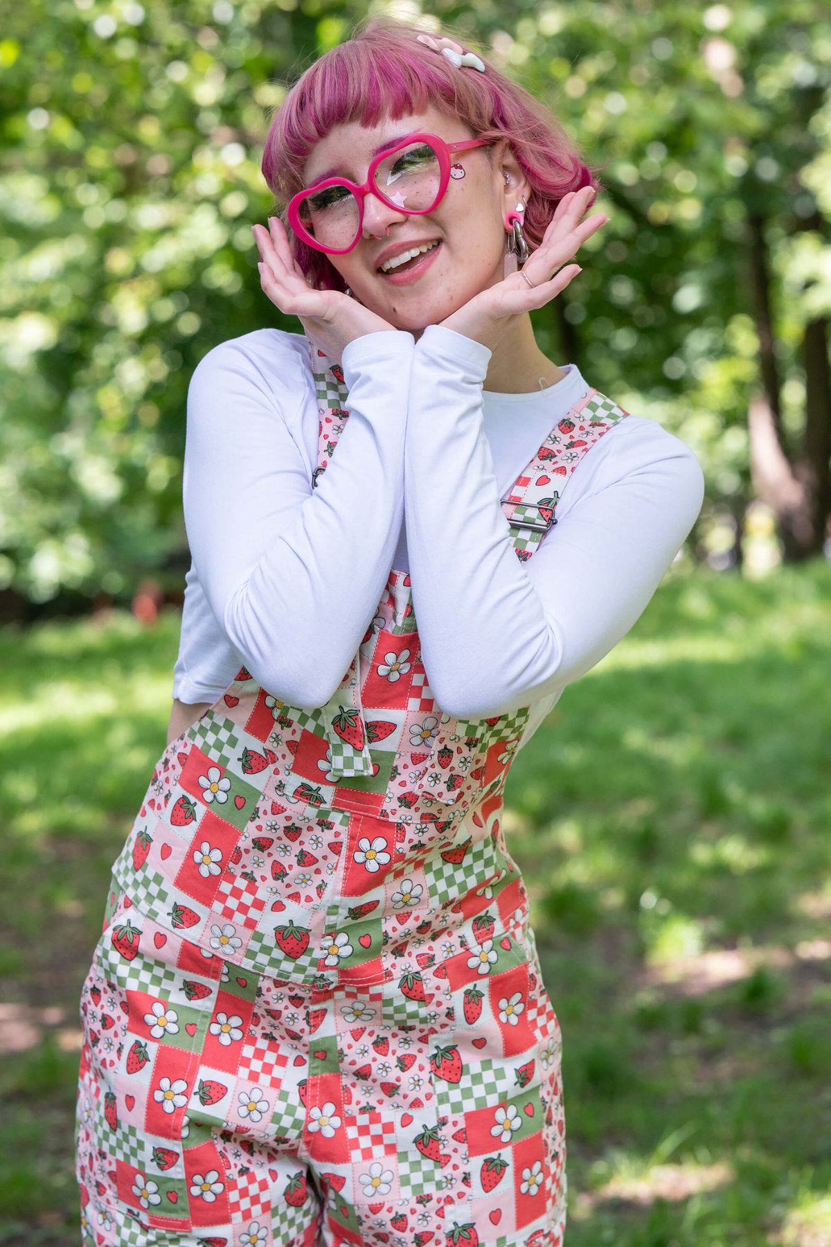 @fairyjesss holder hænderne op til ansigtet i en glad positur iført Strawberry Picnic Dungarees.