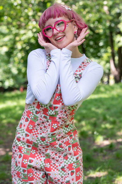 @fairyjesss holder hænderne op til ansigtet i en glad positur iført Strawberry Picnic Dungarees.