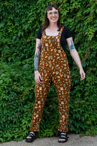 Model iført Rebel Romance Cowboy Stretch Dungarees fra samarbejdet med Yasmin Cousins. Set forfra med grøn baggrund.