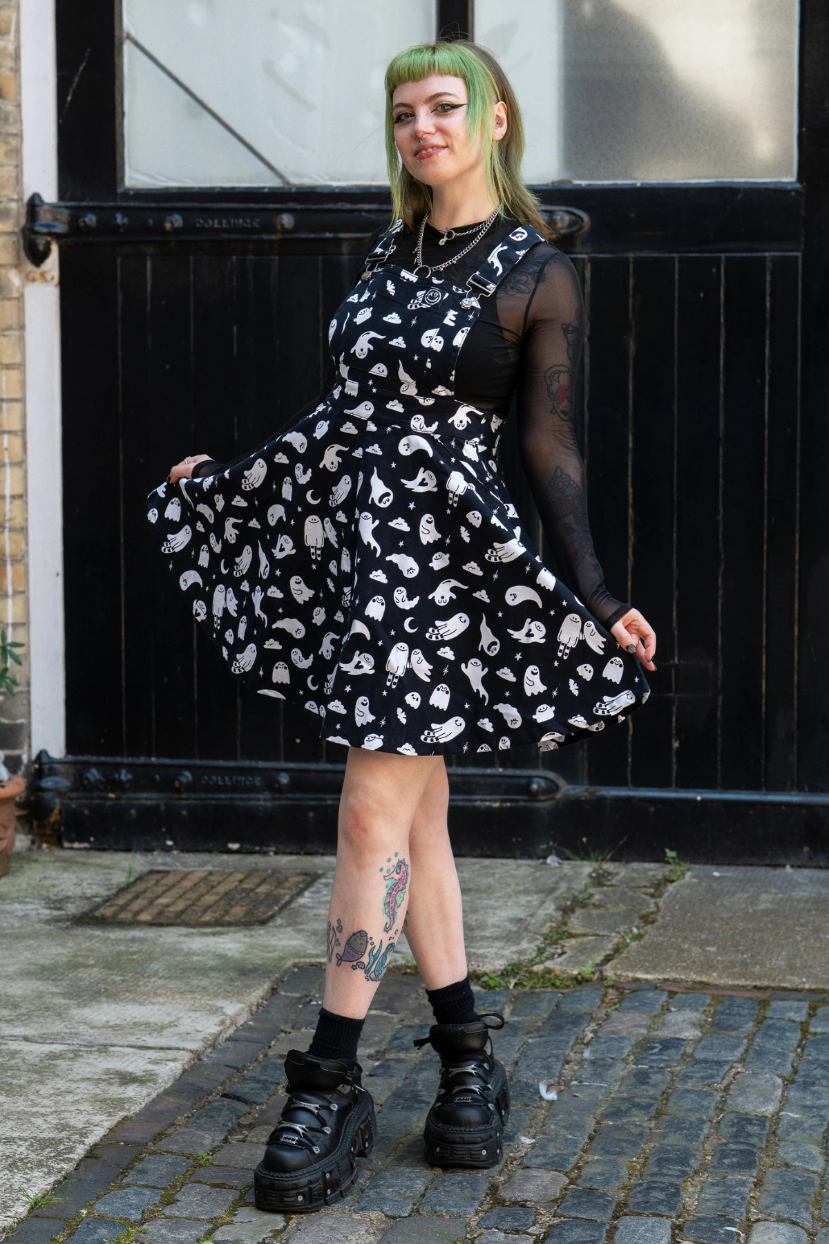 Model iført Rebel Romance x Yasmin Cousins Ghosties Flared Pinafore. Sort kjole med spøgelsesprint og flared nederdel.