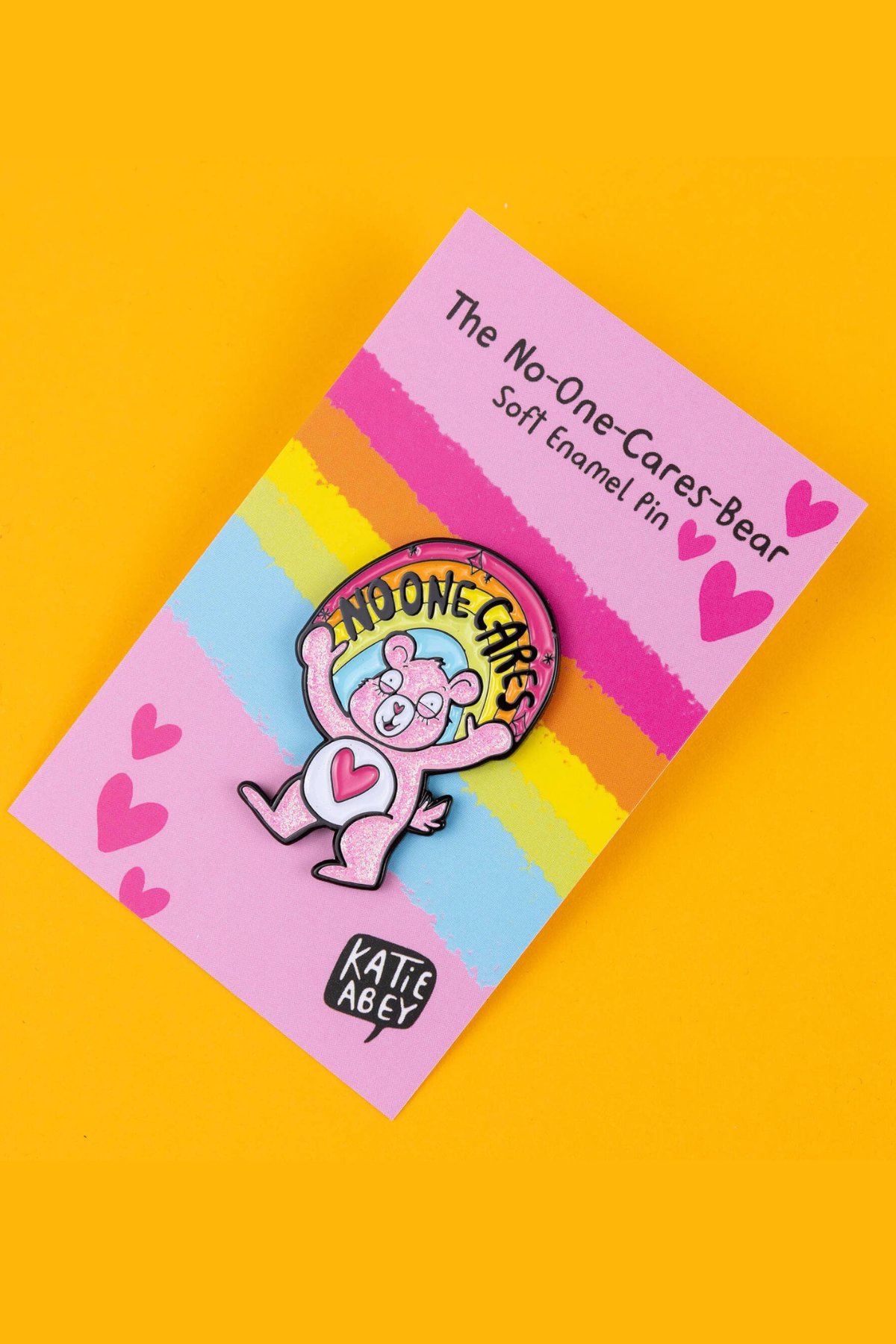 inklet closeup af No-One-Cares Bear soft enamel pin på pink regnbue-backer