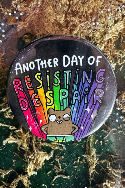 Katie Abey badge med teksten "Another Day of Resisting Despair", regnbuefarver og lille bjørn i underbukser – 58 mm rund badge