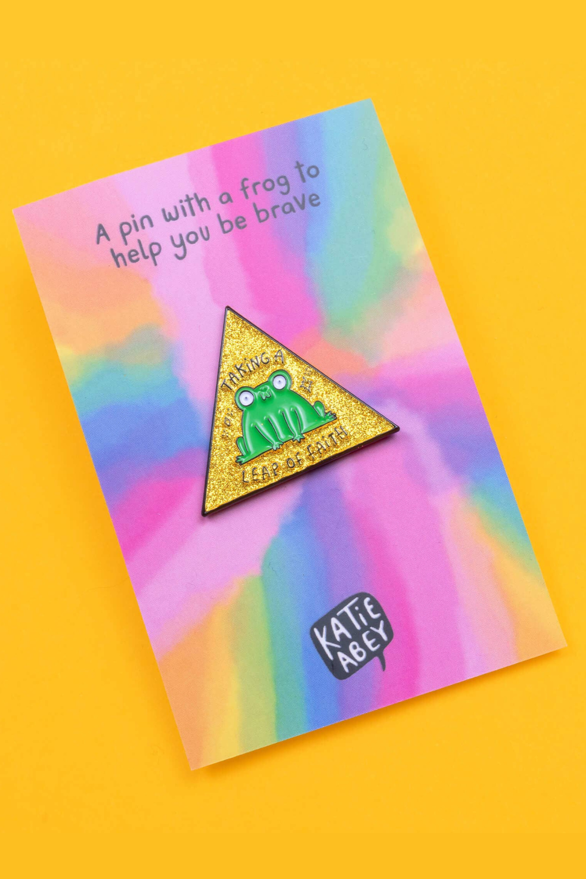 Katie Abey frøpin formet som gylden glitter trekant vist fra siden på backing-card