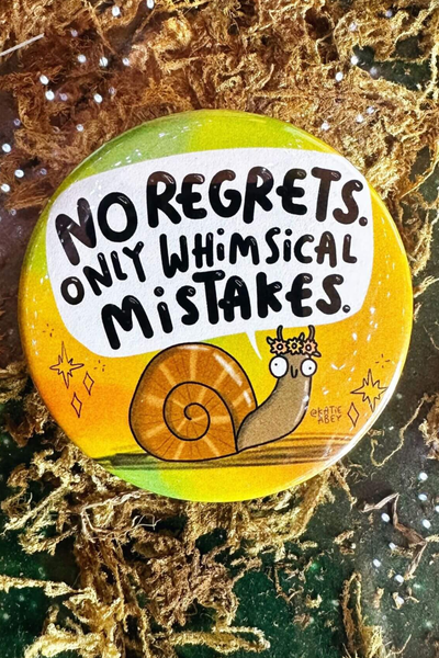 Katie Abey badge med teksten “No Regrets, Only Whimsical Mistakes” og lille snegl med blomsterkrans – 58 mm badge