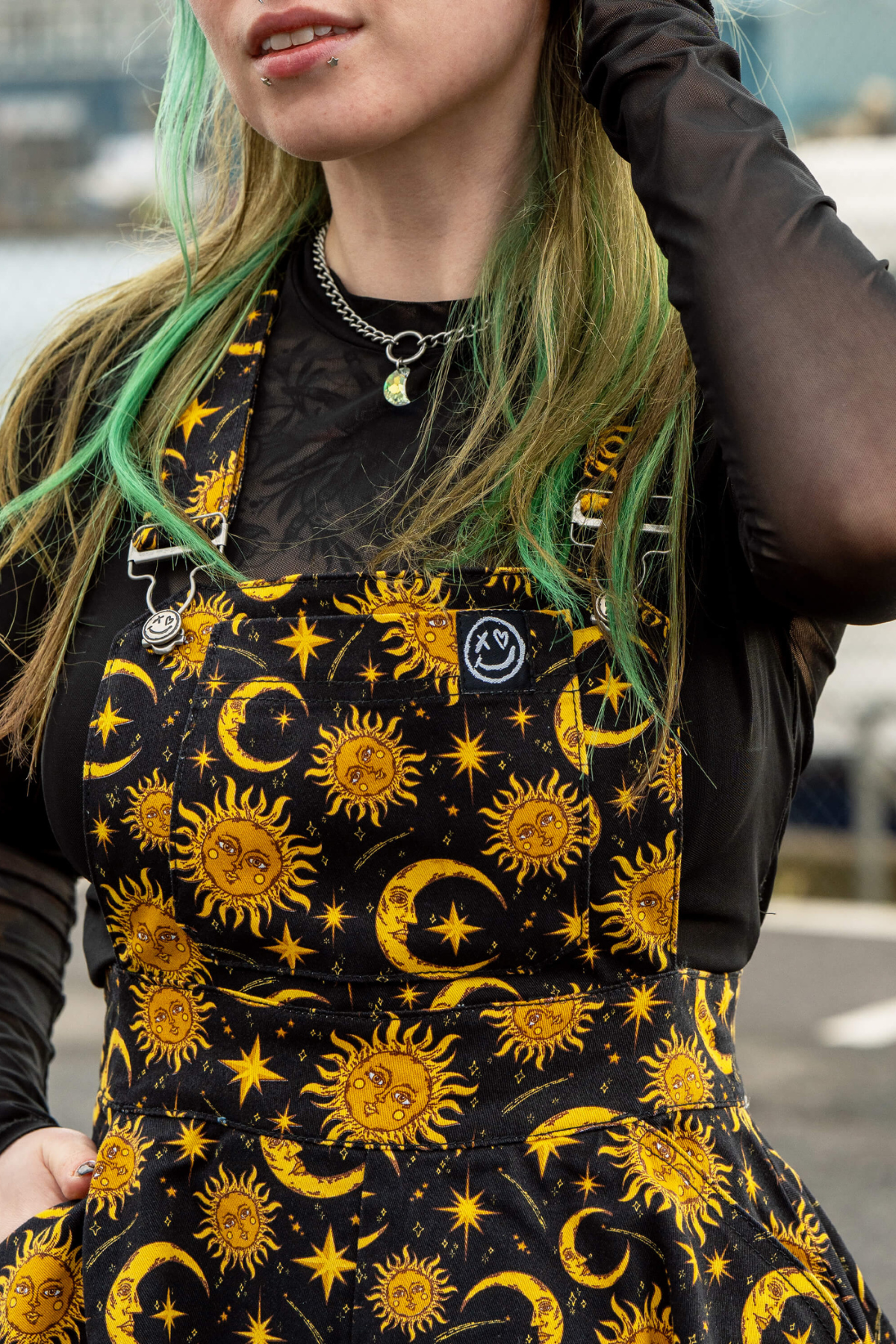 Nærbillede af frontlommeklappen på Rebel Romance Celestial Sun & Moon kjolen – smiley logo og metalspænder.