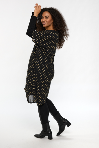 Model i STUDIO Alma Dress bevæger sig i profil, kjolen fanger lyset i de gyldne prikker.