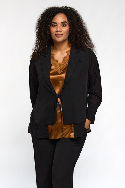 Model iført Ingrid top i kobber fra STUDIO under sort jakke – satinlook med blondekant.